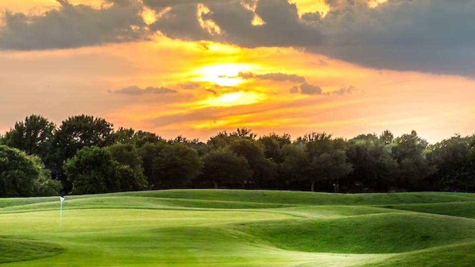Sunset over a green golf course with trees and clouds