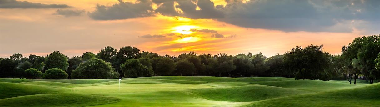 Sunset over a green golf course with trees and clouds